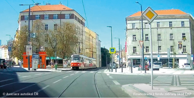 Pohled řidiče na hlavní silnici, v protisměru po kolejích uprostřed vozovky přijíždí tramvaj